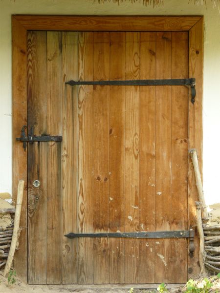 Large wooden door in light brown tone with metal hinges and latch.